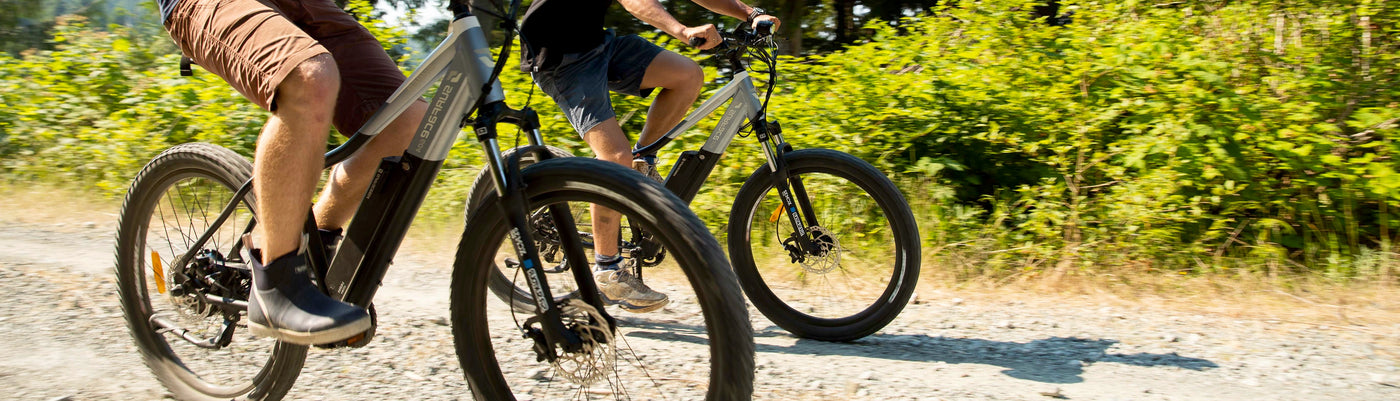 Two individuals riding eBikes on pathway during summer months