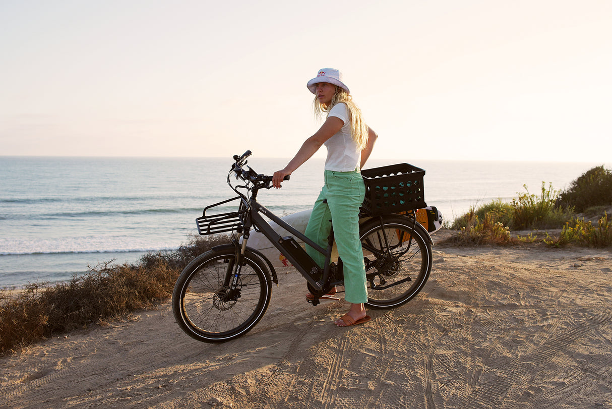 Surface 604 Werk Low-Step Commuter eBike with a surfboard sitting on top of a hill overlooking a beach.